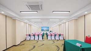 Une salle de conférence avec des rangées de tables, une table verte sur le côté droit et un tableau accroché au mur.