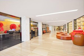 Un hall d’hôtel moderne avec un sol ciré, un comptoir d’accueil et un grand vase décoratif.