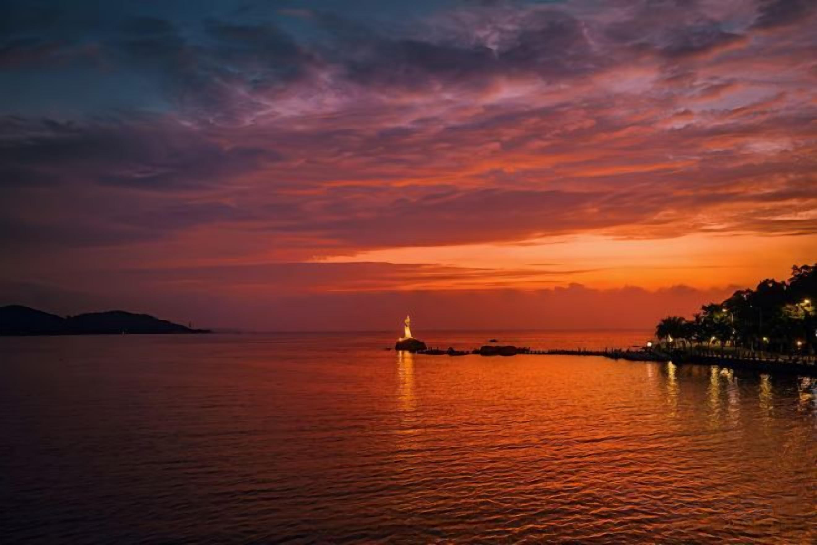 A sunset over a calm body of water with a distant shoreline.