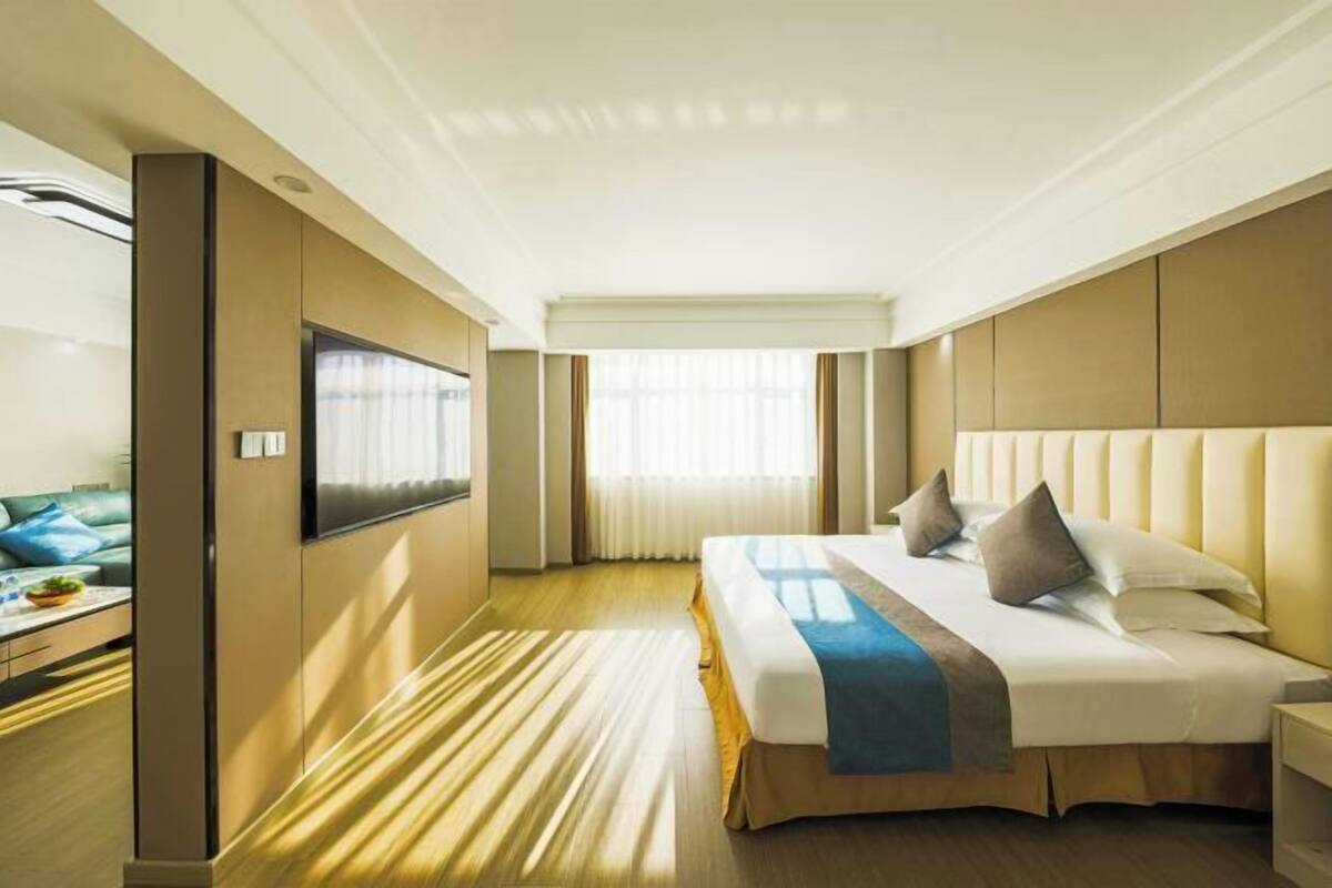 A hotel room with a large bed, a flat-screen TV, a desk, and a window with curtains.