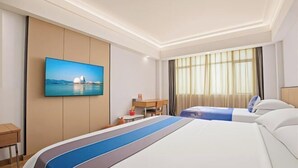 Habitación de hotel con cama, escritorio, silla, televisor montado en la pared y ventana con cortinas.