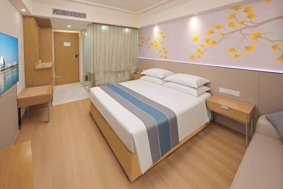 A modern hotel room with a large bed, a bedside table, a nightstand, and a wall-mounted TV.