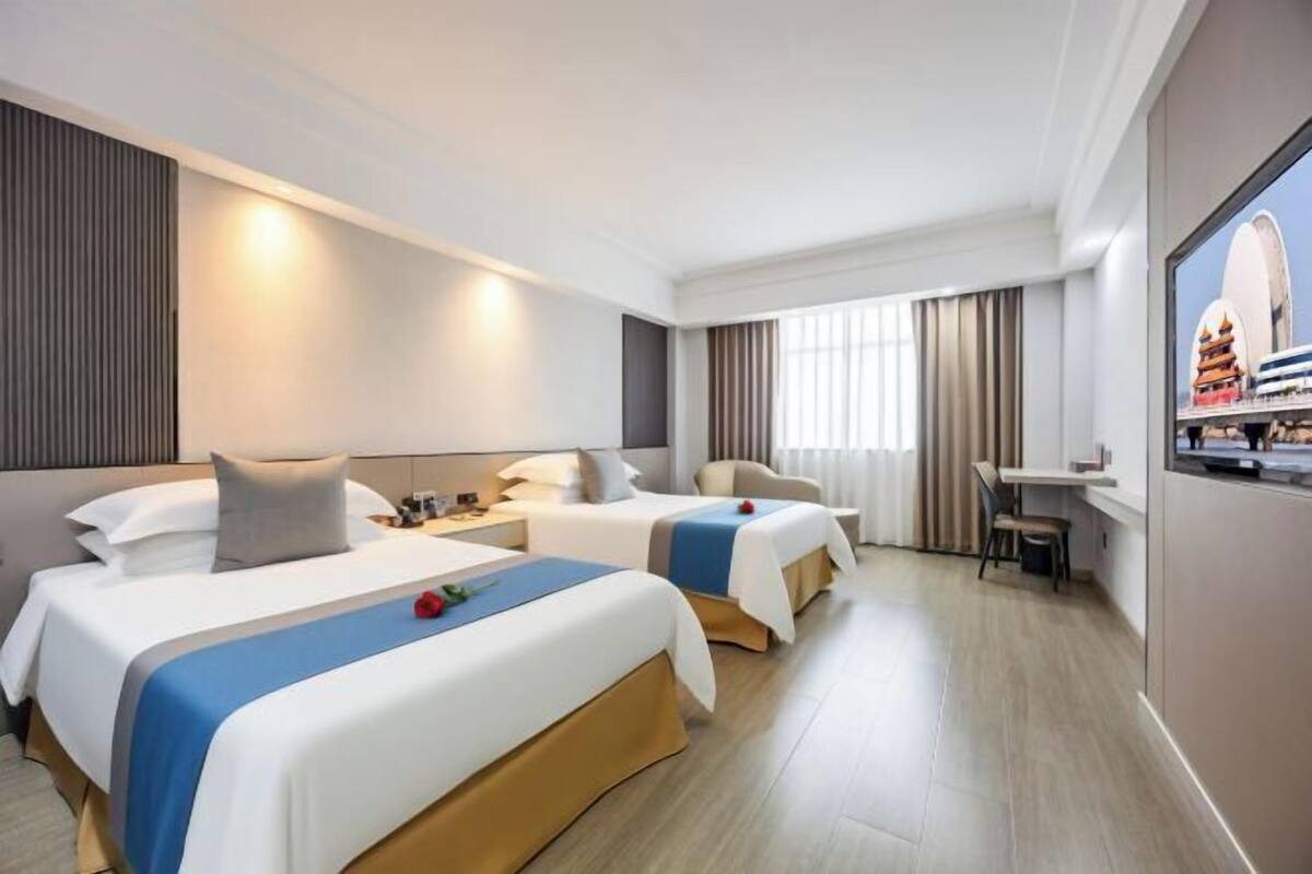 A hotel room with two beds, a desk, a chair, and a large window.