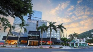 Un hotel con fachada de vidrio moderna, palmeras en primer plano y cielo despejado.
