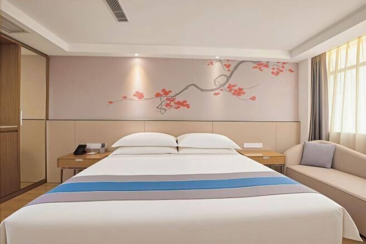 A hotel room with a large bed, a bedside table, a nightstand, a sofa, and a wall with a floral mural.