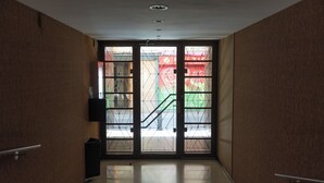 Un pasillo con una puerta de vidrio que da al exterior, un bote de basura y una barandilla a la izquierda.