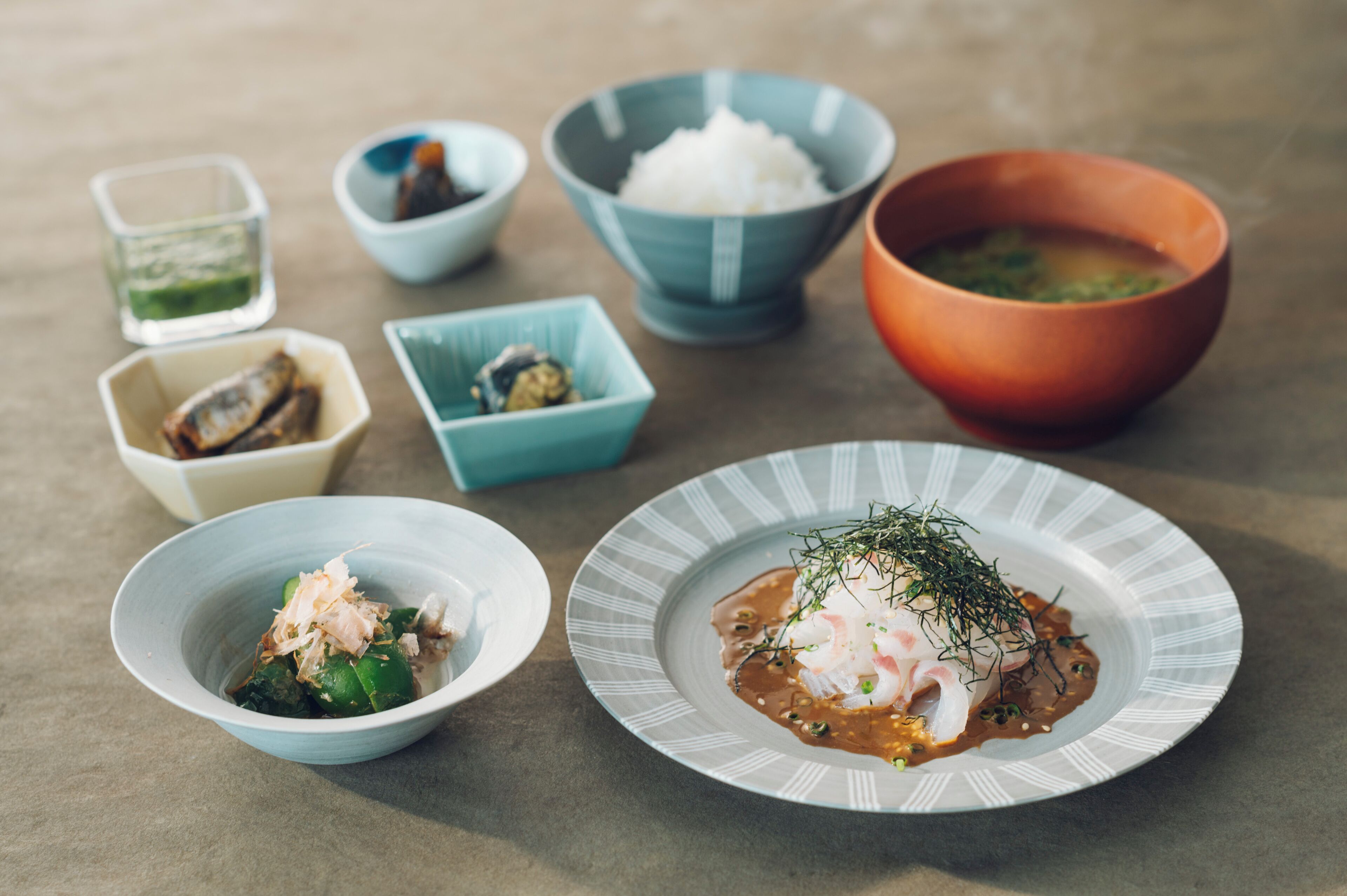 A variety of dishes including a plate with fish and greens, bowls of rice, and small dishes with different ingredients.