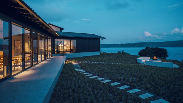 A modern house with large glass windows, a fire pit, and a view of the water. - Kikka Hirado (Hirado)