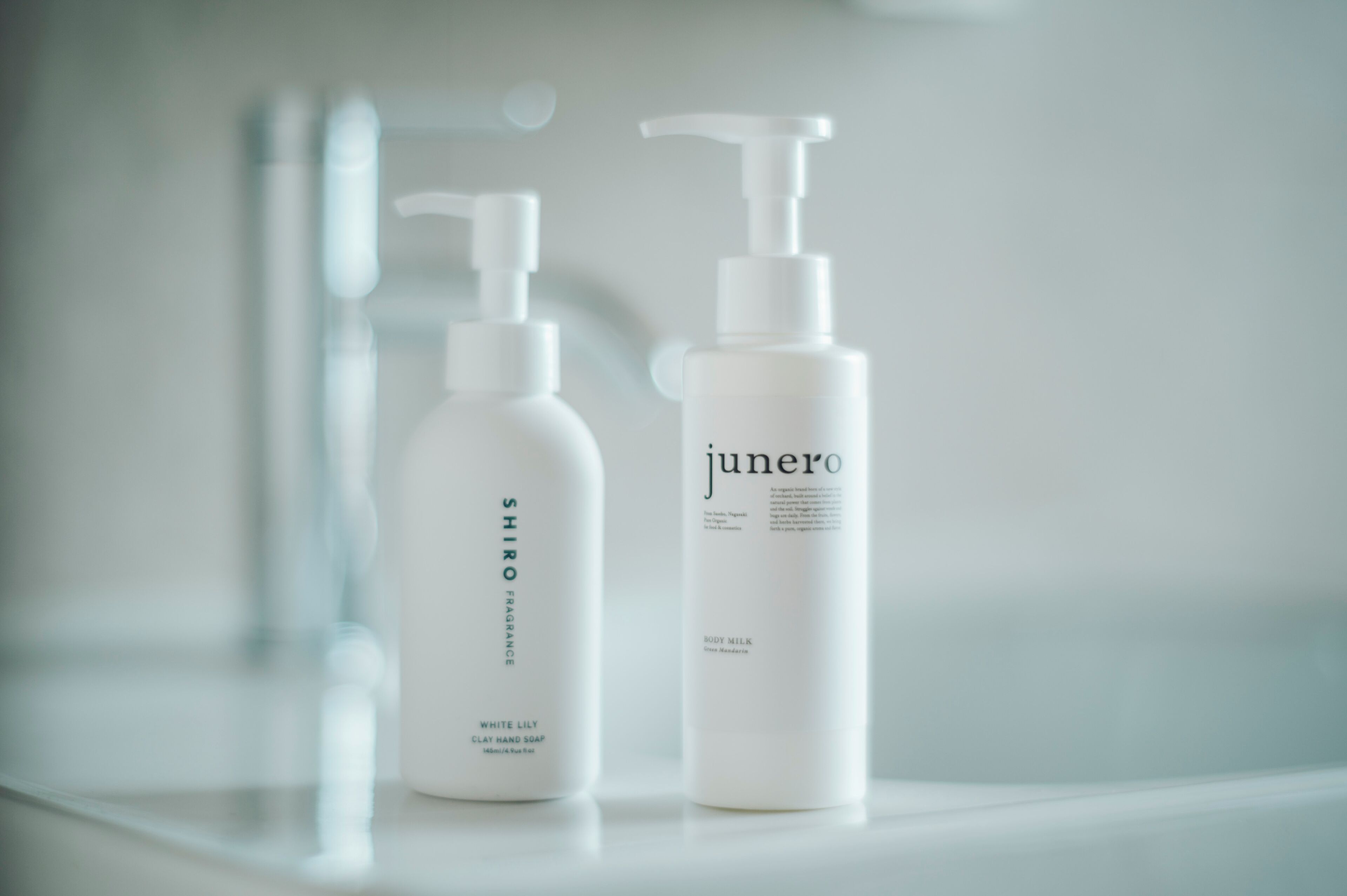 Two white bottles of Shiro and Junero body care products on a reflective surface.