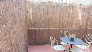 A patio with a woven bamboo fence, a round table with chairs, and a potted plant. - Sweet BCN Studio with Terrace (Barcelona)