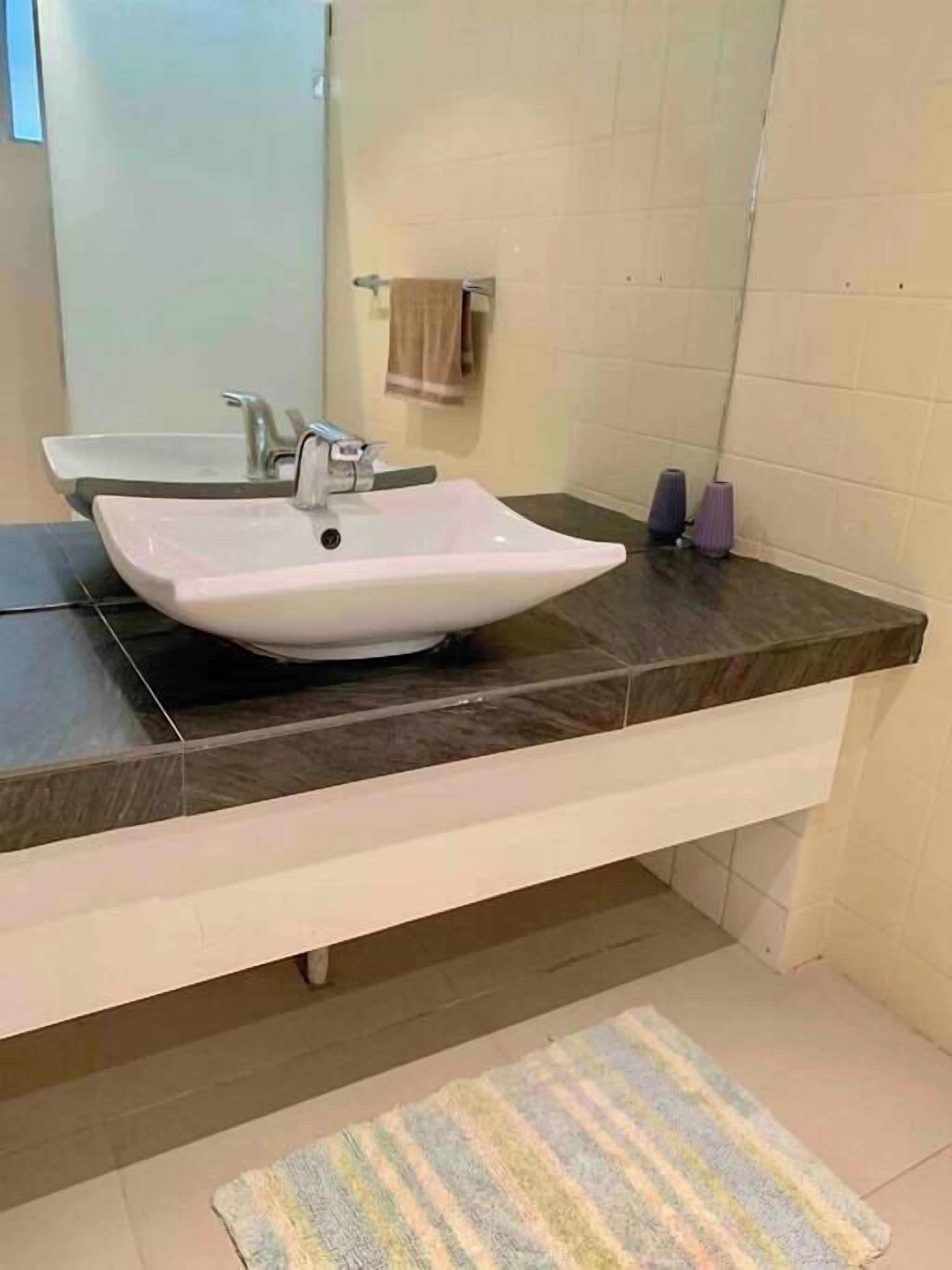 Un baño con lavamanos blanco, encimera oscura y un felpudo a rayas en el suelo.