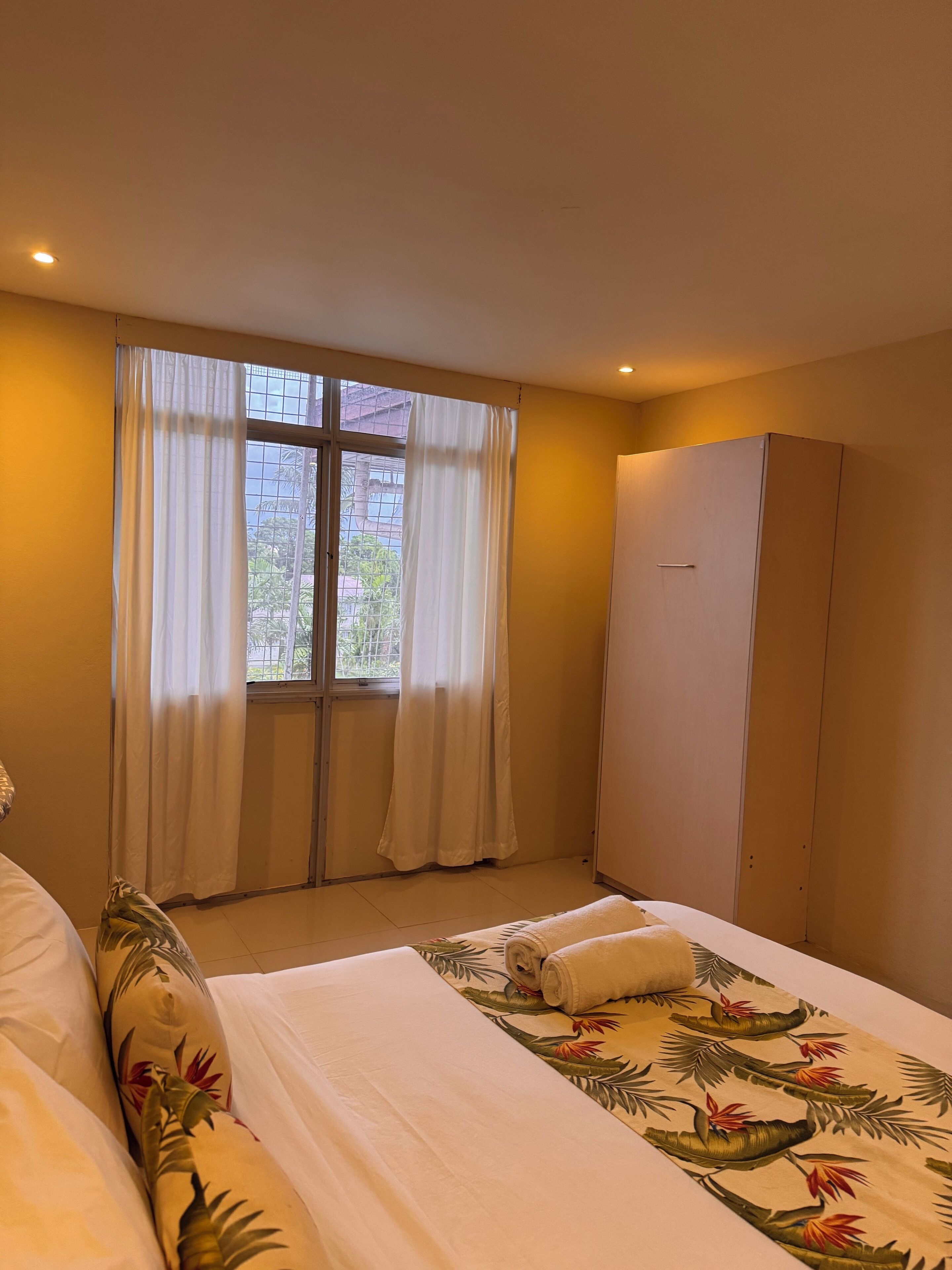 A hotel room with a bed, a wardrobe, and a window with curtains.