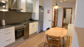 A modern kitchen with stainless steel appliances, a wooden dining table, and a built-in oven. - Sweet BCN Plaza Universidad (Barcelona)