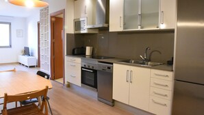 A modern kitchen with stainless steel appliances, a dining area with a wooden table and chairs, and a view of the outside through a window. - Sweet BCN Plaza Universidad (Barcelona)