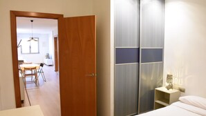 A hotel room with a wooden door, a bed, a bedside table with a lamp, and a wardrobe with a mirror. - Sweet BCN Plaza Universidad (Barcelona)