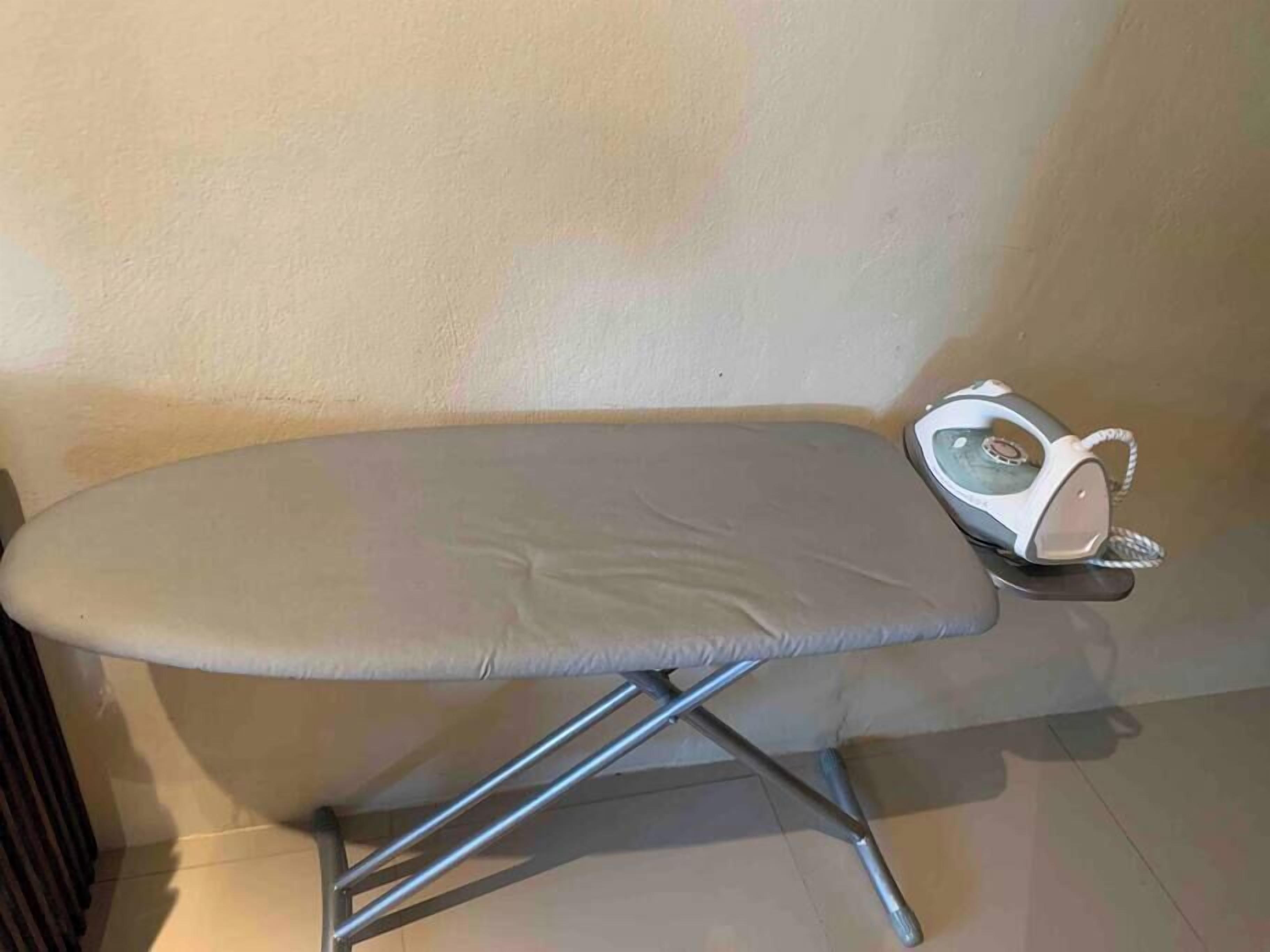 A compact, foldable ironing board with a metallic frame and a grey surface, placed against a plain wall.