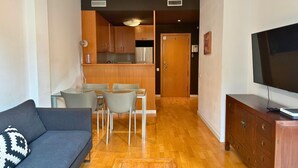 A modern living room with a grey sofa, a dining area with a glass table and chairs, a wooden cabinet with a TV, and a kitchen in the background. - Sweet BCN Rambla 48. (Barcelona)