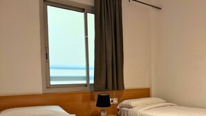 A hotel room with two beds, a window with curtains, a bedside lamp, and a view of the sea. - Sweet BCN Rambla 48. (Barcelona)