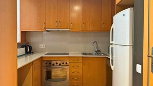 A compact kitchen with wooden cabinets, a stainless steel oven, a white refrigerator, and a microwave. - Sweet BCN Rambla 48. (Barcelona)
