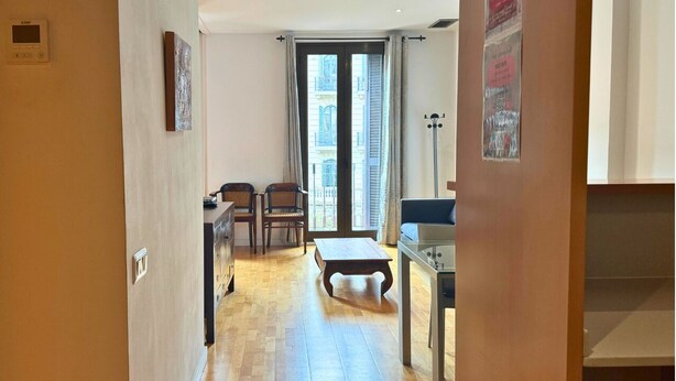 A room with a wooden floor, a dining table with chairs, a sofa, and a window with curtains. - Sweet BCN Rambla 48. (Barcelona)