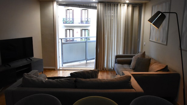 Ett vardagsrum med en soffa, en tv, en golvlampa och en balkong med gardiner.
