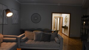 Ett vardagsrum med en grå soffa, en svart fåtölj och en golvlampa. Längre bak i rummet står ett matbord med stolar.
