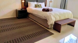 A modern hotel room with a large bed, a bedside table, a lamp, and a patterned rug.