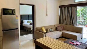 A modern hotel room with a kitchenette, a sofa, a small table, and a view of greenery through the window.