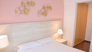 Ein ordentlich bezogenes Bett mit weißen Leinen, zwei Nachttischlampen und ein helles Kopfende in einem Zimmer mit rosafarbenen Wänden und einer Holztür.
