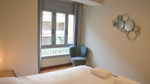 Ein Hotelzimmer mit einem großen Bett, einem Sessel und einem Fenster mit Blick auf Balkone.