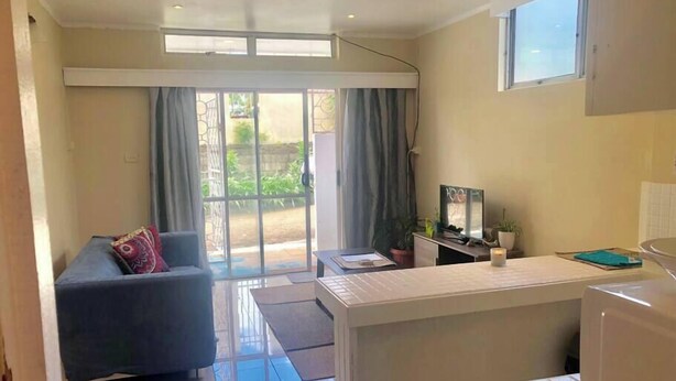 A modern living room with a sofa, a coffee table, and a TV. There is a sliding glass door leading to a garden.