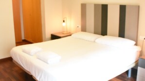 Un letto rifatto con lenzuola e cuscini bianchi, una lampada da comodino e un pavimento in legno.