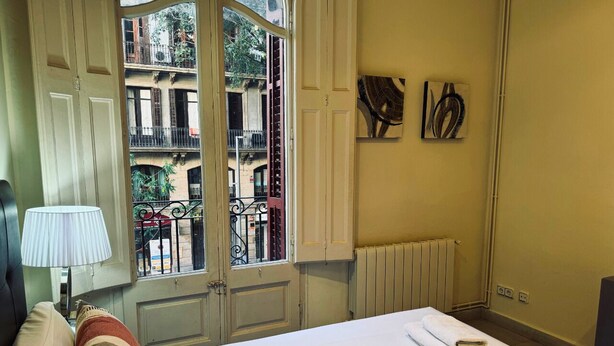 Ein Hotelzimmer mit einem Bett, einem Fenster mit Blick auf Gebäude, einem Heizkörper und einem an der Wand hängenden Kunstwerk.