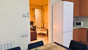 Eine kompakte Küche mit Kühlschrank, Mikrowelle und Holzschränken. Im Vordergrund steht ein Esstisch mit Stühlen.