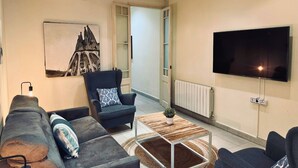 Ein modernes Wohnzimmer mit Sofa, Sessel und Couchtisch, einem Flachbildfernseher und einem Gemälde eines Gebäudes.
