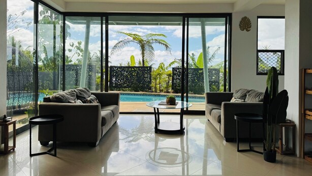 A spacious living room with a large glass wall offering a view of a pool and tropical plants.