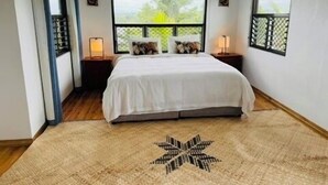 A bedroom with a bed, two bedside tables, a window, and a decorative rug.