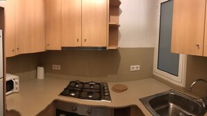 A compact kitchen with wooden cabinets, a gas stove, a microwave, and a sink. - TWO-BEDROOM APARTMENT (Barcelona)