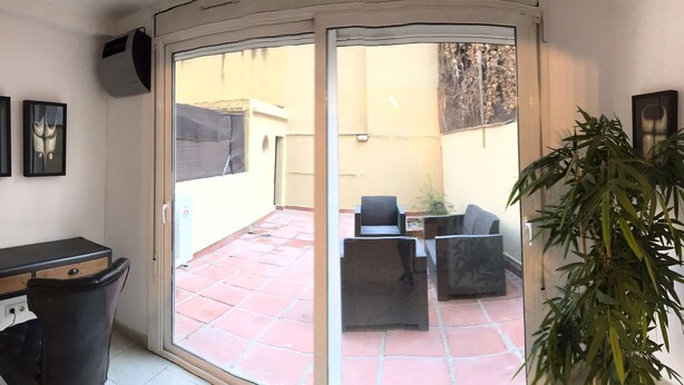 A room with a sliding glass door leading to an outdoor patio with a table and chairs, a potted plant, and a radiator. - TWO-BEDROOM APARTMENT (Barcelona)