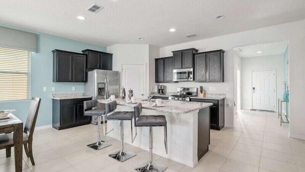 A modern kitchen with dark cabinets, a central island with bar stools, and a dining area with a table and chairs.
