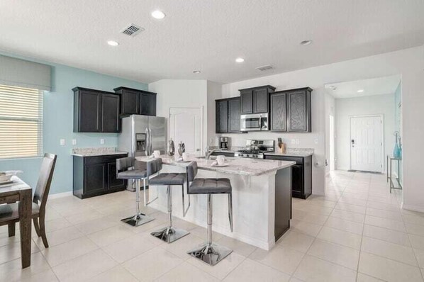 A modern kitchen with dark cabinets, a central island with bar stools, and a dining area with a table and chairs.