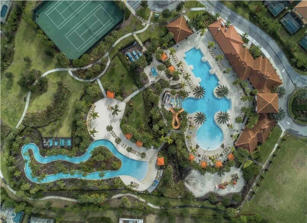 An aerial view of a resort with a large central pool, a tennis court, and a winding water feature.