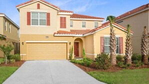 A two-story house with a garage, a red-tiled roof, and a front yard with palm trees.
