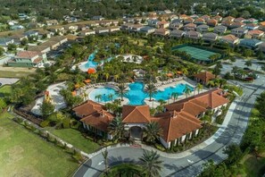 An aerial view of a residential area with a central swimming pool surrounded by houses, palm trees, and a tennis court. - Solterra Family Paradise-5261 (Davenport)
