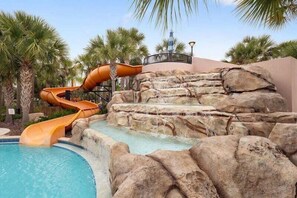 A pool with a water slide and rock formations.