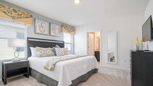 A bedroom with a large bed, bedside tables, a dresser, and a television.