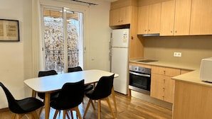 A compact kitchen with a dining table, chairs, a refrigerator, oven, and wooden cabinets.
