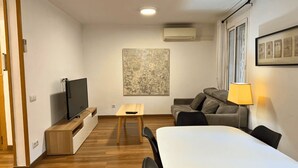A modern living room with a flat-screen TV, a wooden coffee table, a sofa, and a dining table.