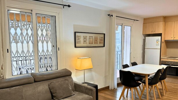 A living room with a sofa, a dining table with chairs, a lamp, and a kitchen area with cabinets and a refrigerator.