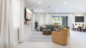 En moderne stue med sofa, sofabord og et fjernsyn monteret på væggen.